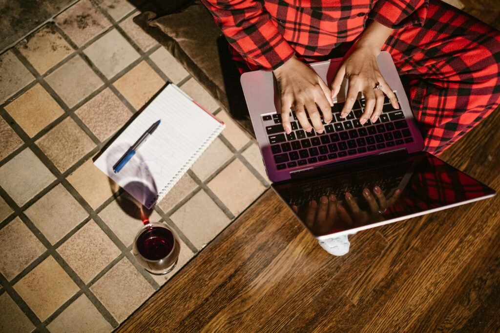 A person typing on a computer with a glass of wine beside them.